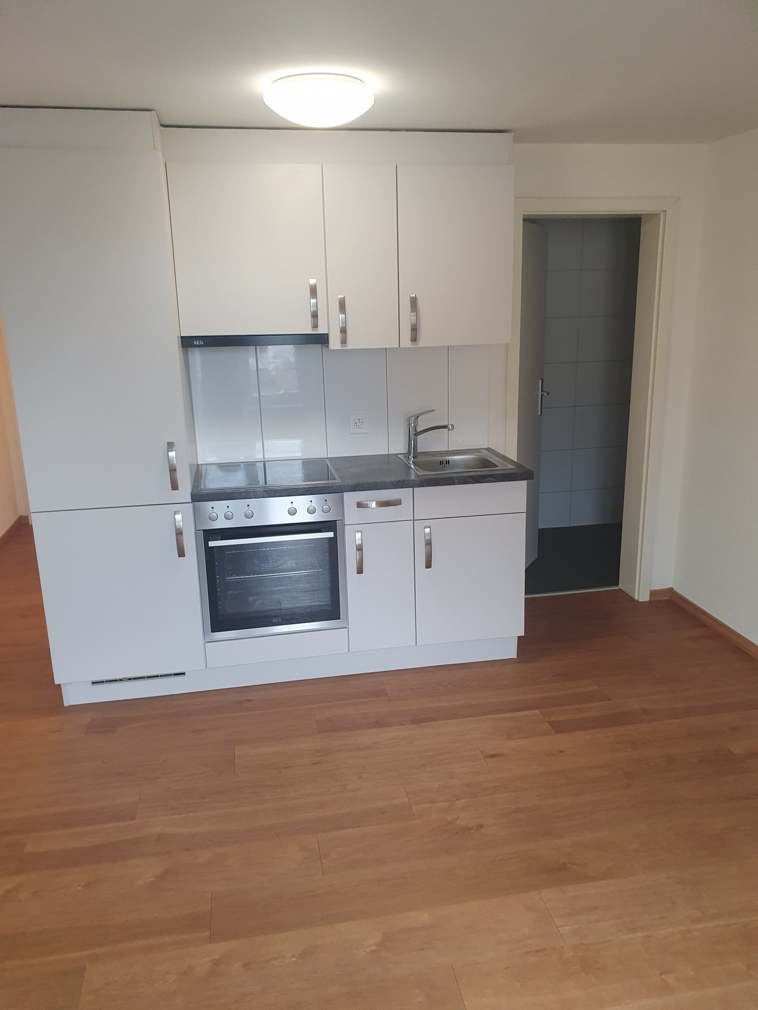 Modern kitchen with white cabinets, stainless steel appliances including an oven and dishwasher, and hardwood flooring.