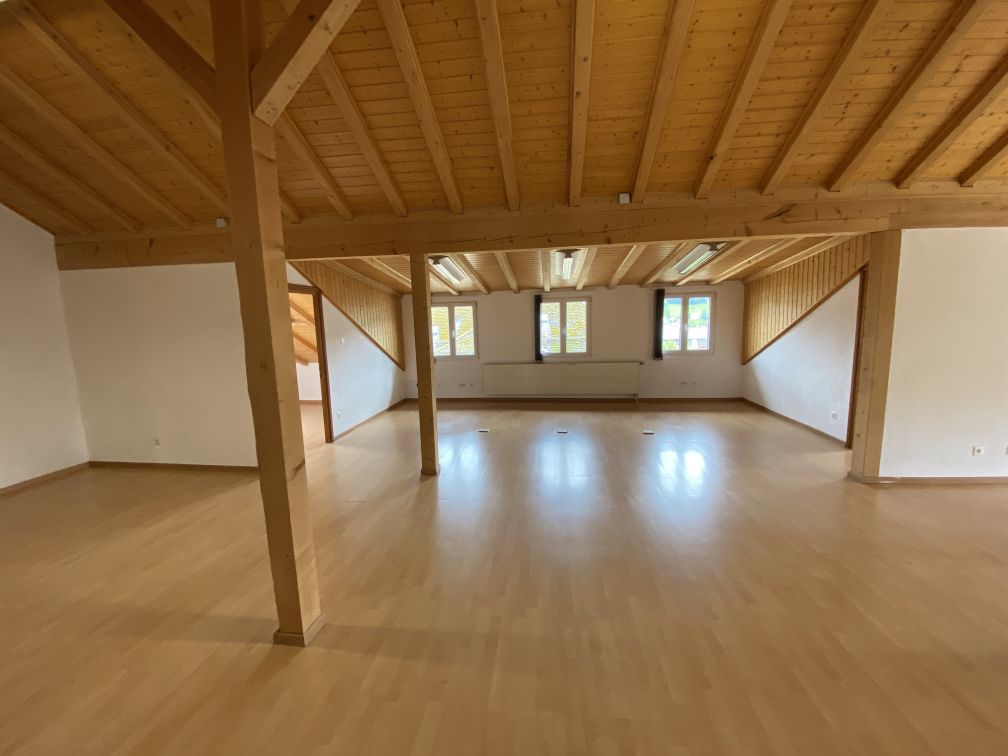 Large open space with wooden beamed ceiling, hardwood floors, and multiple windows providing natural light. The room appears to be a studio or multipurpose space.