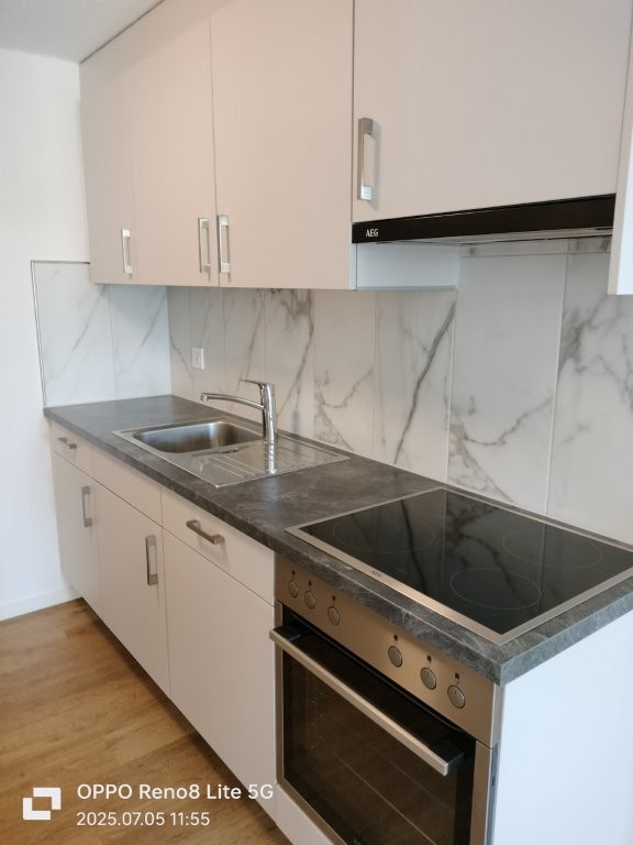 Modern kitchen with light-colored cabinets, marble-like backsplash, built-in oven and dishwasher, and a double sink with a faucet.