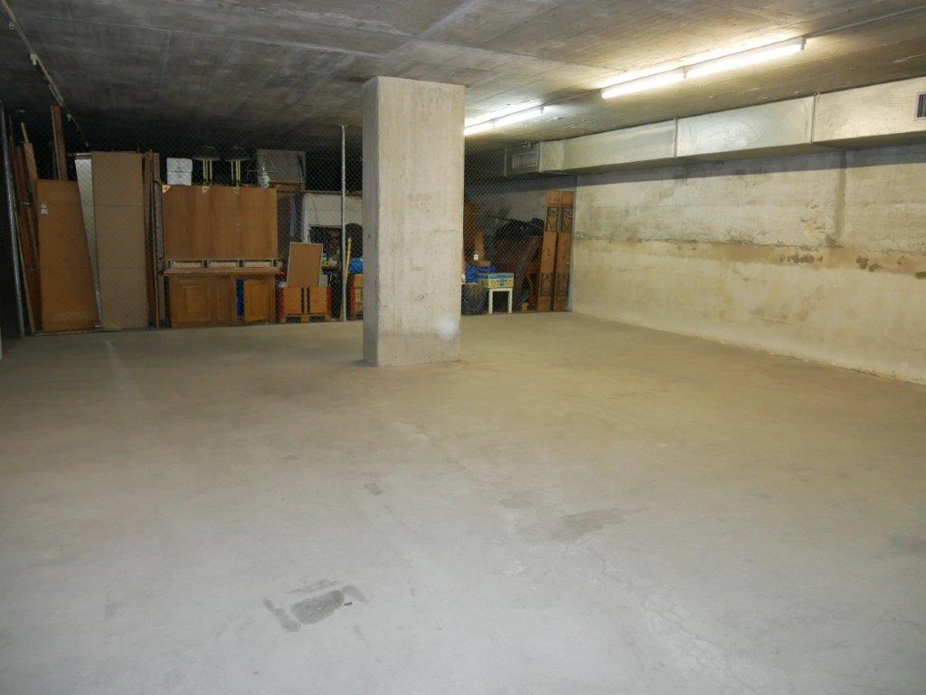 Large open basement space with concrete floor, exposed ceiling, and storage boxes and furniture items along the walls.
