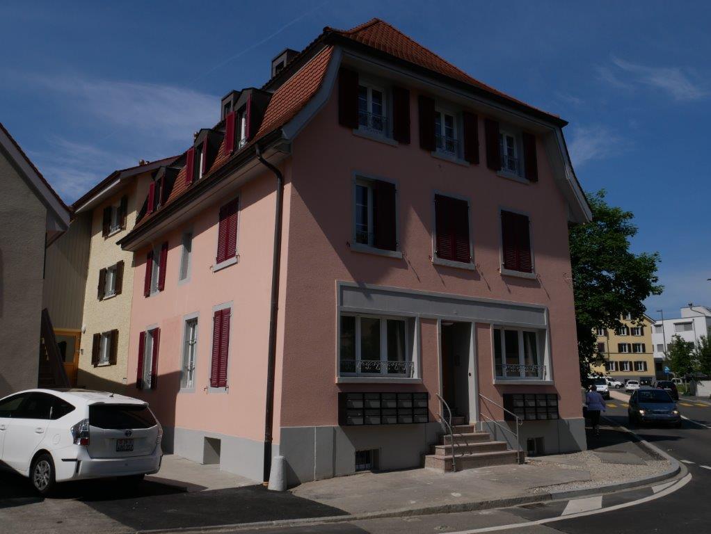3 story house, painted pink, red shutters, street corner, parked car