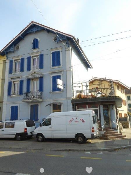 2 story building, blue shutters, balcony, stairs to entrance, adjacent cafe building, parked vans in front
