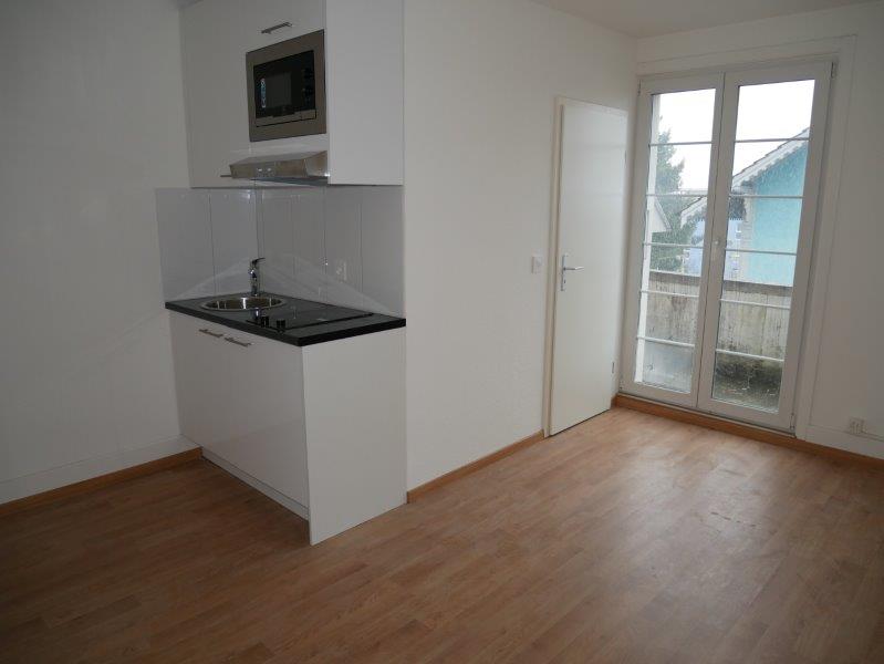 Empty room with a small kitchen area, including a sink, microwave, and a cabinet.