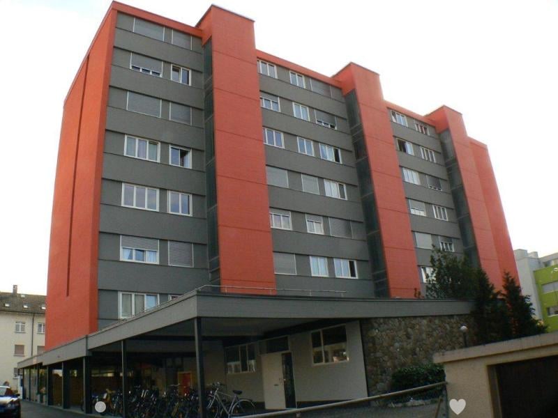 Red and gray building with many windows, covered parking lot, bicycles parked in front