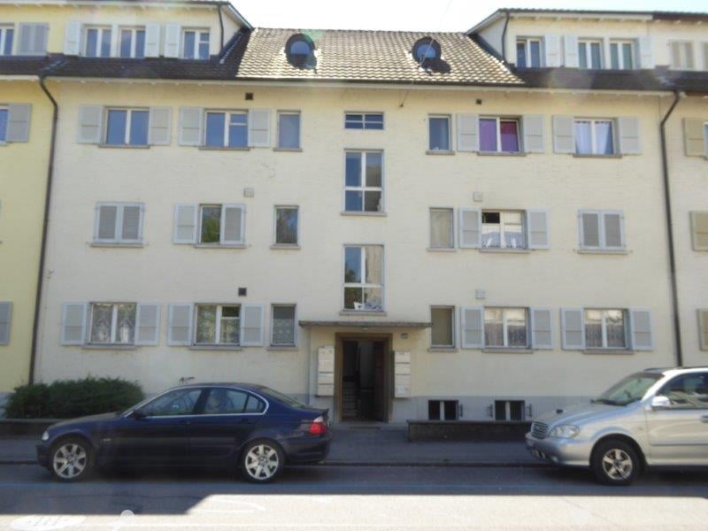 4 story yellow building, white shutters on windows, front door, cars parked in front