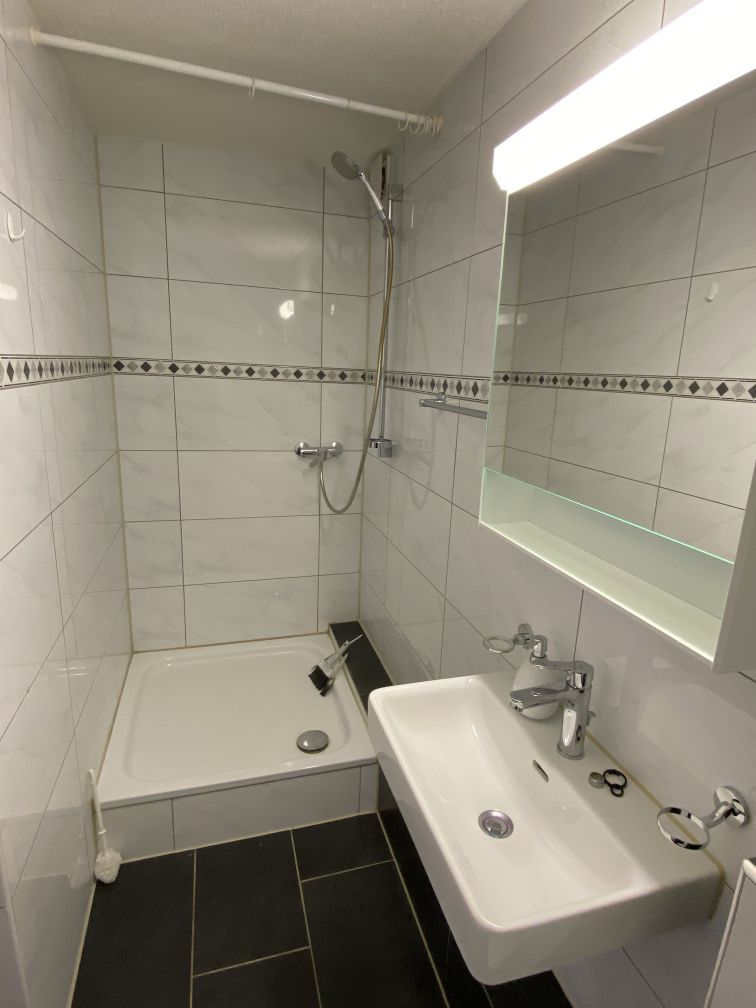 modern and clean bathroom, shower, sink, mirror, white tiled walls, black floor tiles