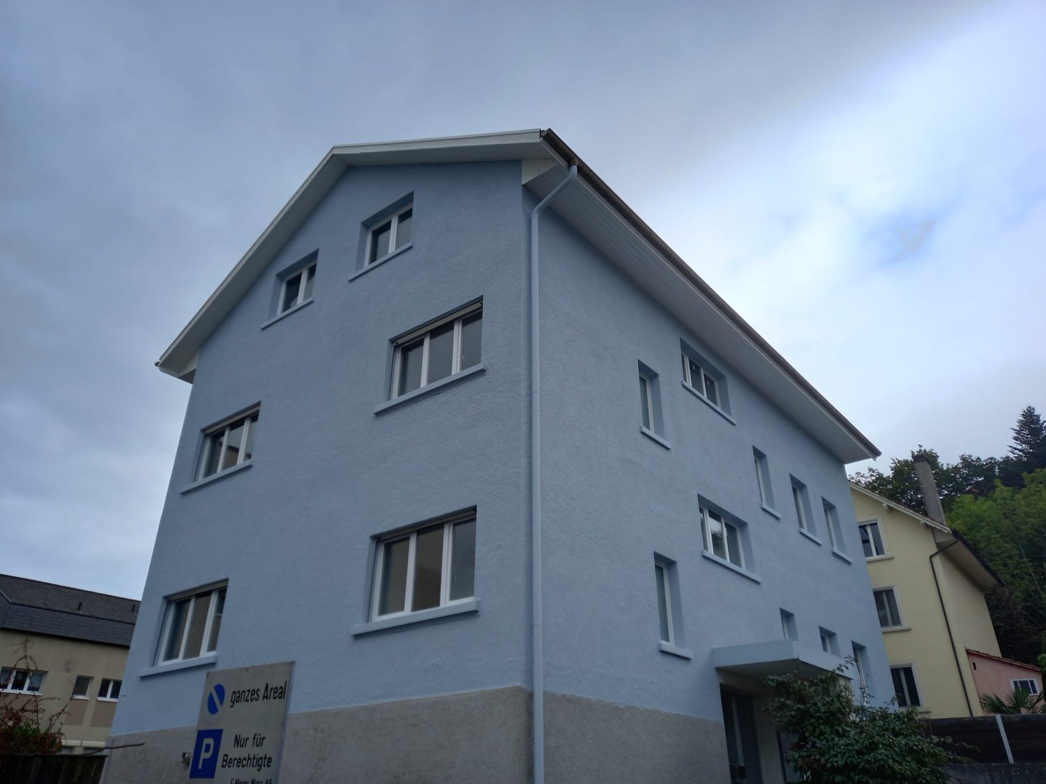 Large blue apartment building with windows, roof gutter, gray foundation, sign reading 'Nur für Berechtigte' on the left side