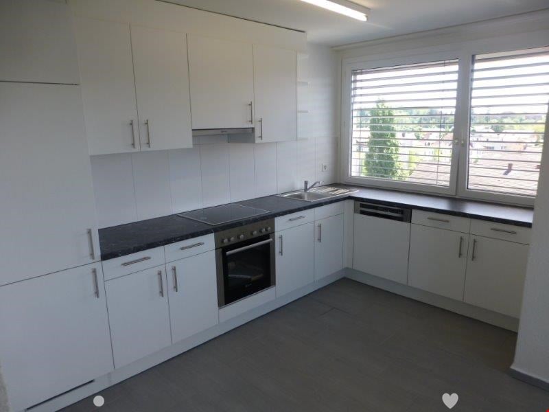 Spacious modern kitchen with white cabinets, black countertops, built-in oven, and dishwasher. Large windows provide natural light and a view of the outdoors.