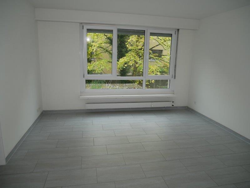 An empty room with a large window, gray tiles, white walls, and white ceiling. There is a white heater under the window.