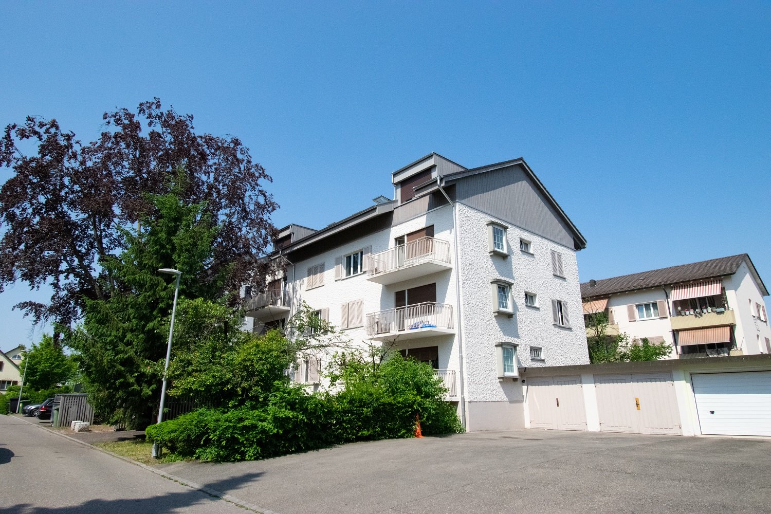 Three story building, white exterior, balconies, multiple garages