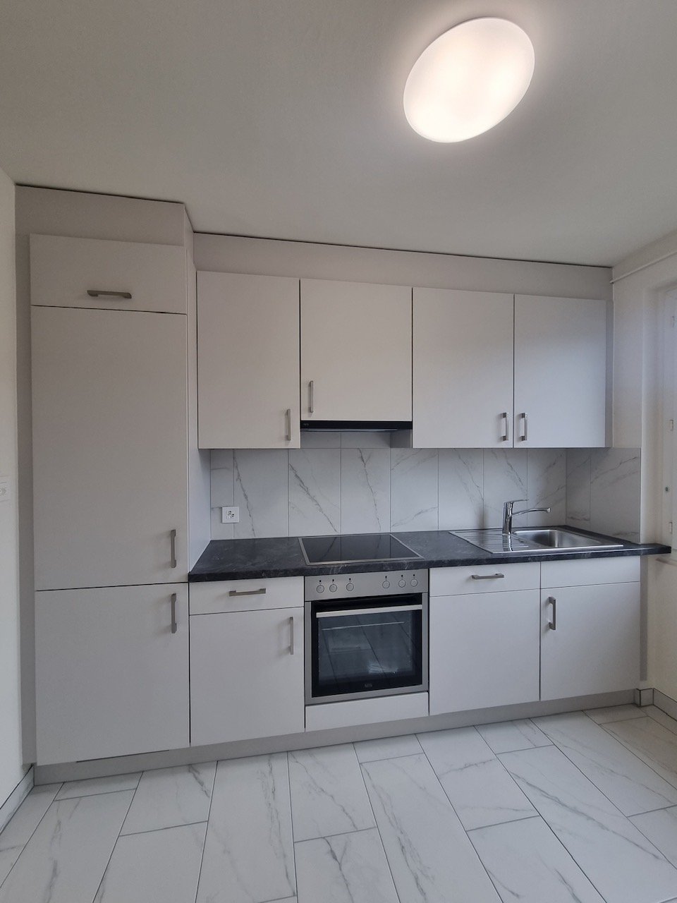 Modern kitchen with white cabinets, marble-patterned backsplash, black countertop, built-in oven, and a dishwasher