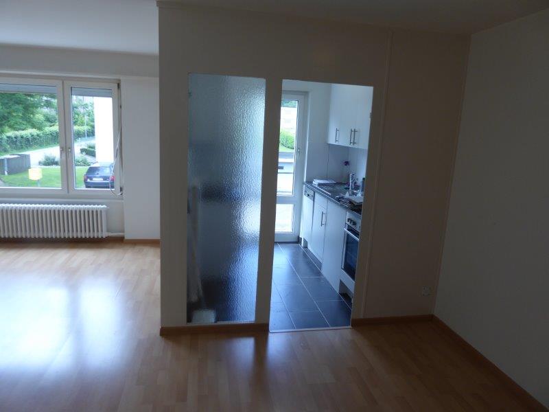 a bright, empty room with wooden floor and large windows with view to a car parked outside
