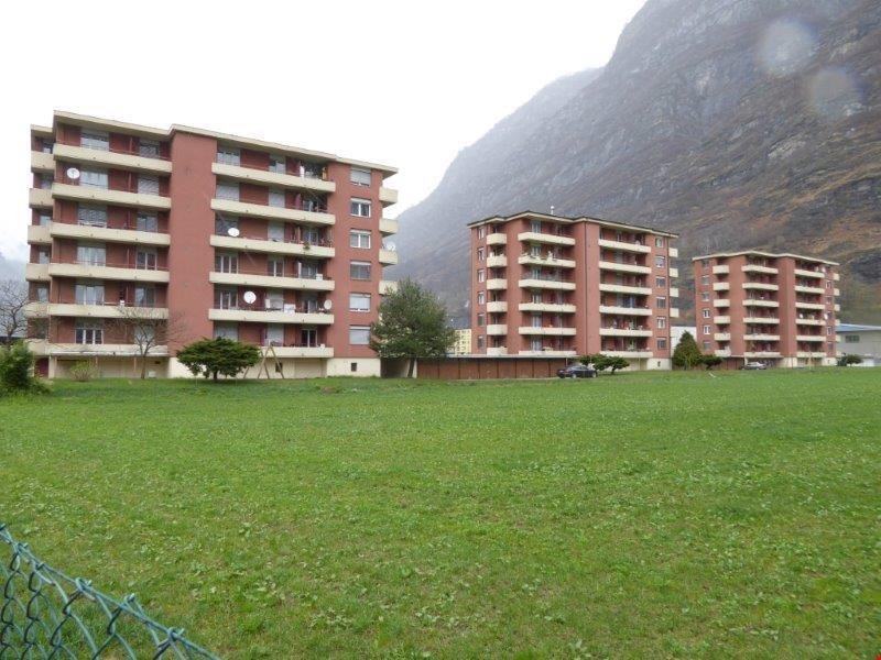 Three red buildings, large field in front, trees, fenced, mountains in the background