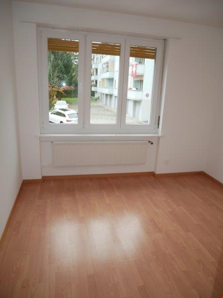 Empty room with wooden floors, large window, heater