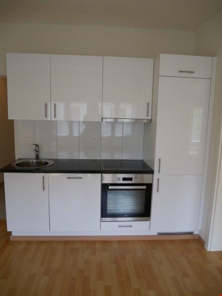 Modern kitchen with white cabinets, black countertop, stainless steel sink, built-in oven, and tiled floor.
