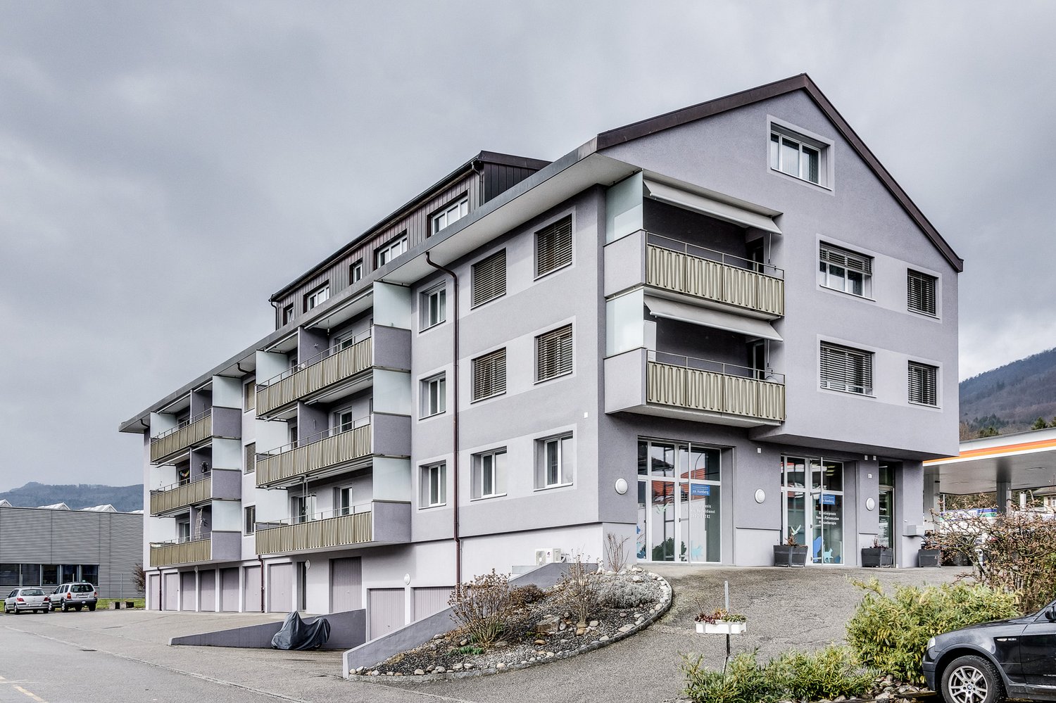 Multi-storey building with multiple balconies and windows, car parking area in front
