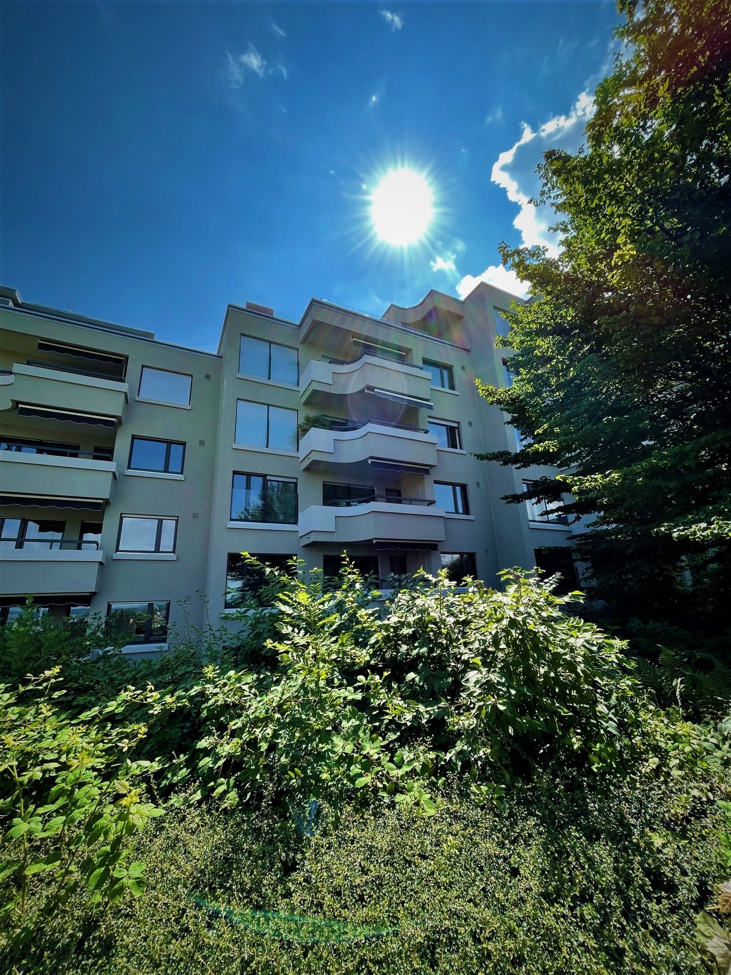 Multi-story building, multiple balconies, surrounded by greenery