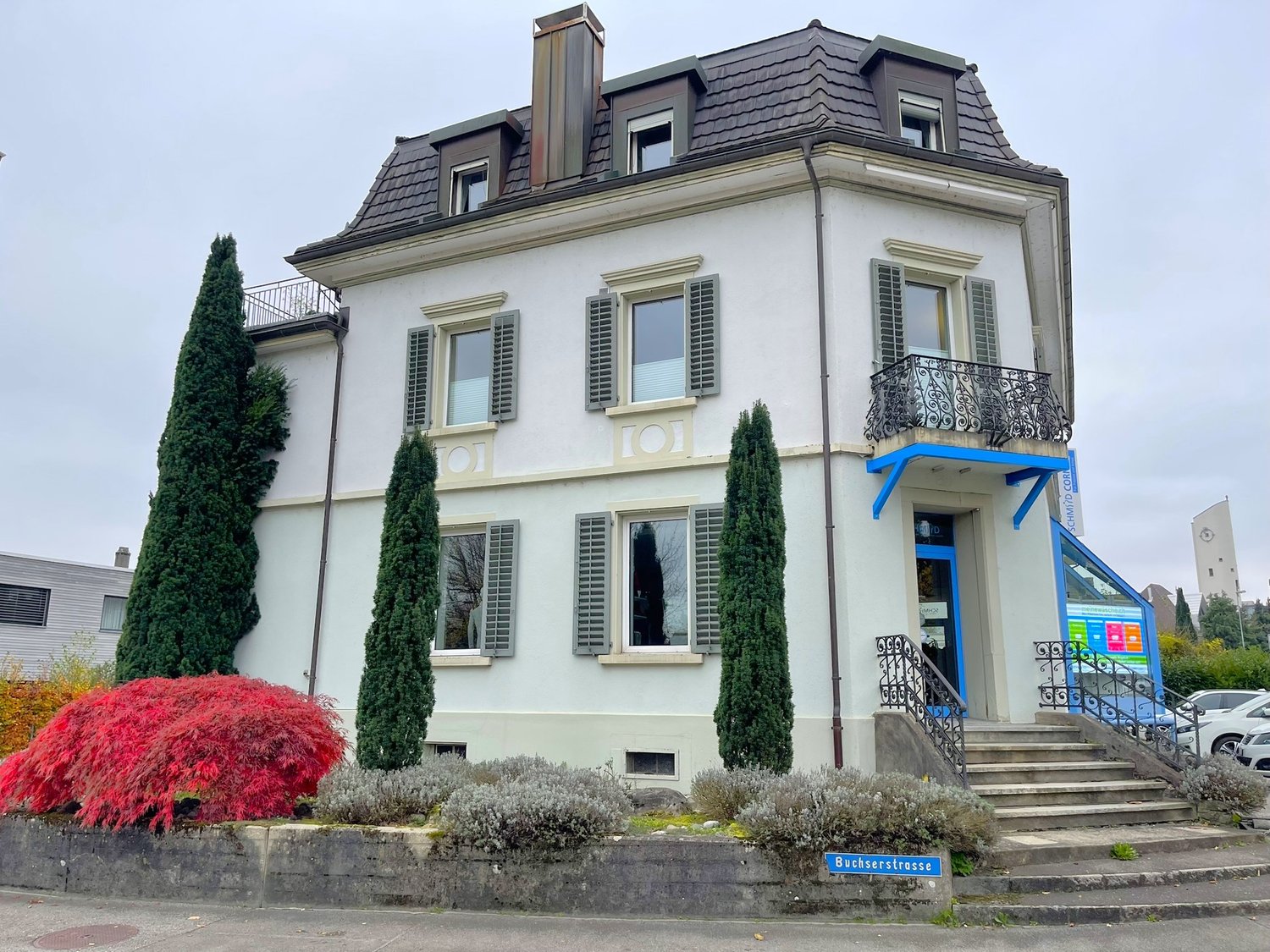 white building, 3 stories, multiple windows, balcony on second floor, entrance stairs