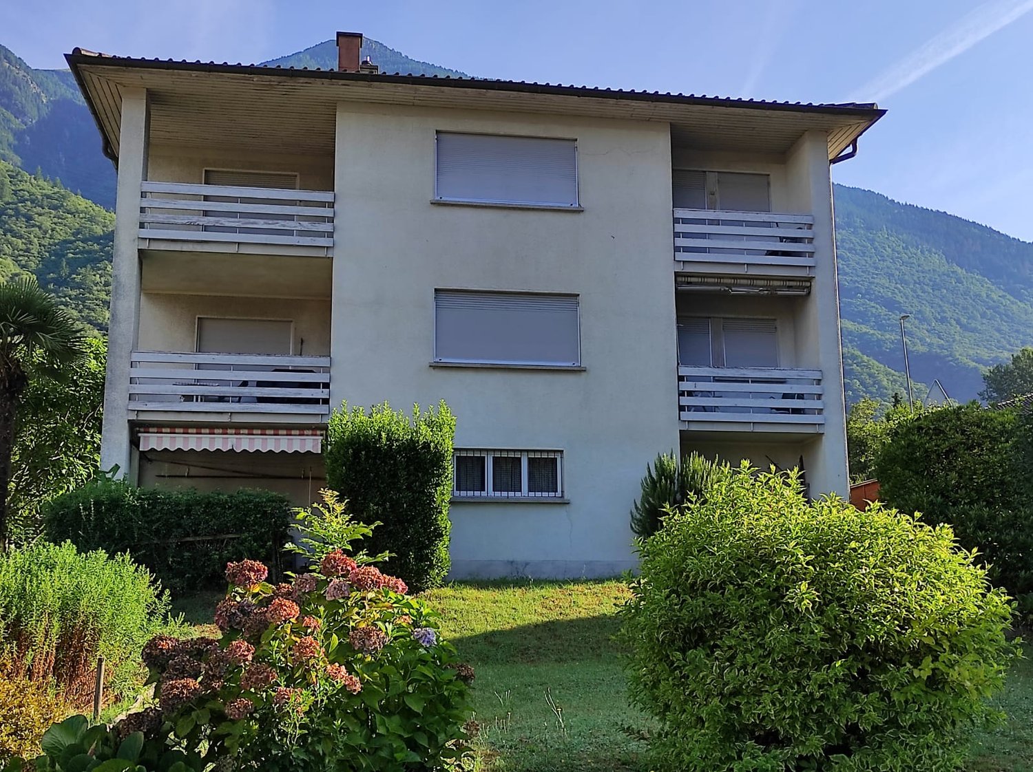 2-story apartment building with balconies, surrounded by lush greenery and gardens