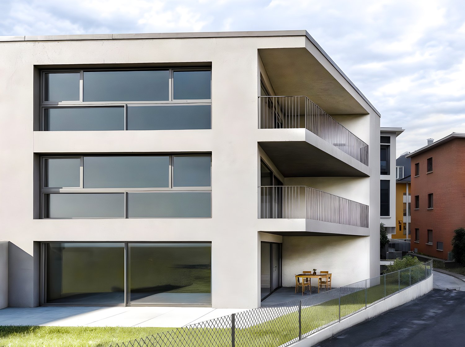 3-story modern apartment building with large windows, balconies, and a small outdoor seating area on the ground floor