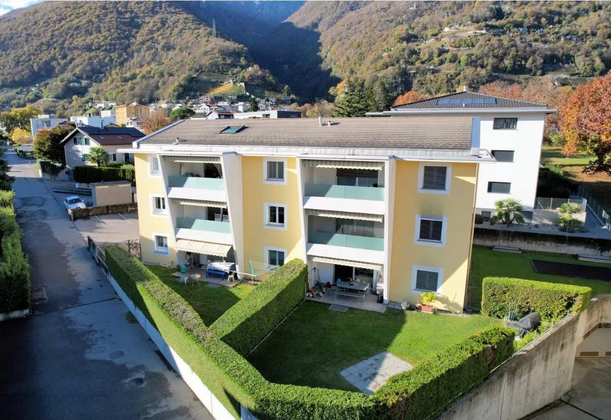 3-story apartment building, yellow exterior, multiple balconies, green hedges, solar panels on the roof, mountain view