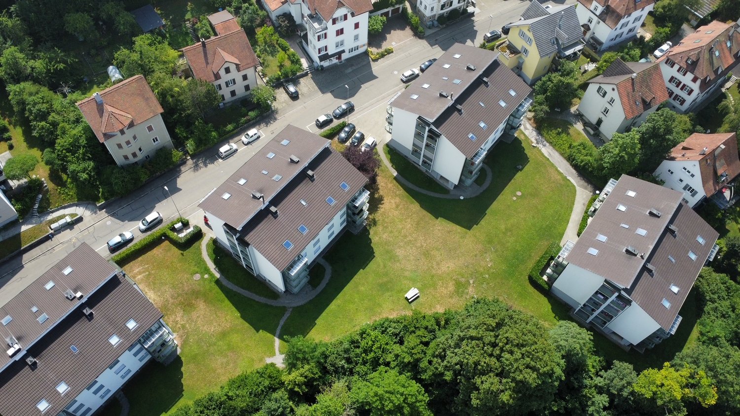 Aerial view of a residential neighborhood with multi-story apartment buildings, houses, and a central grassy area with parking spaces.