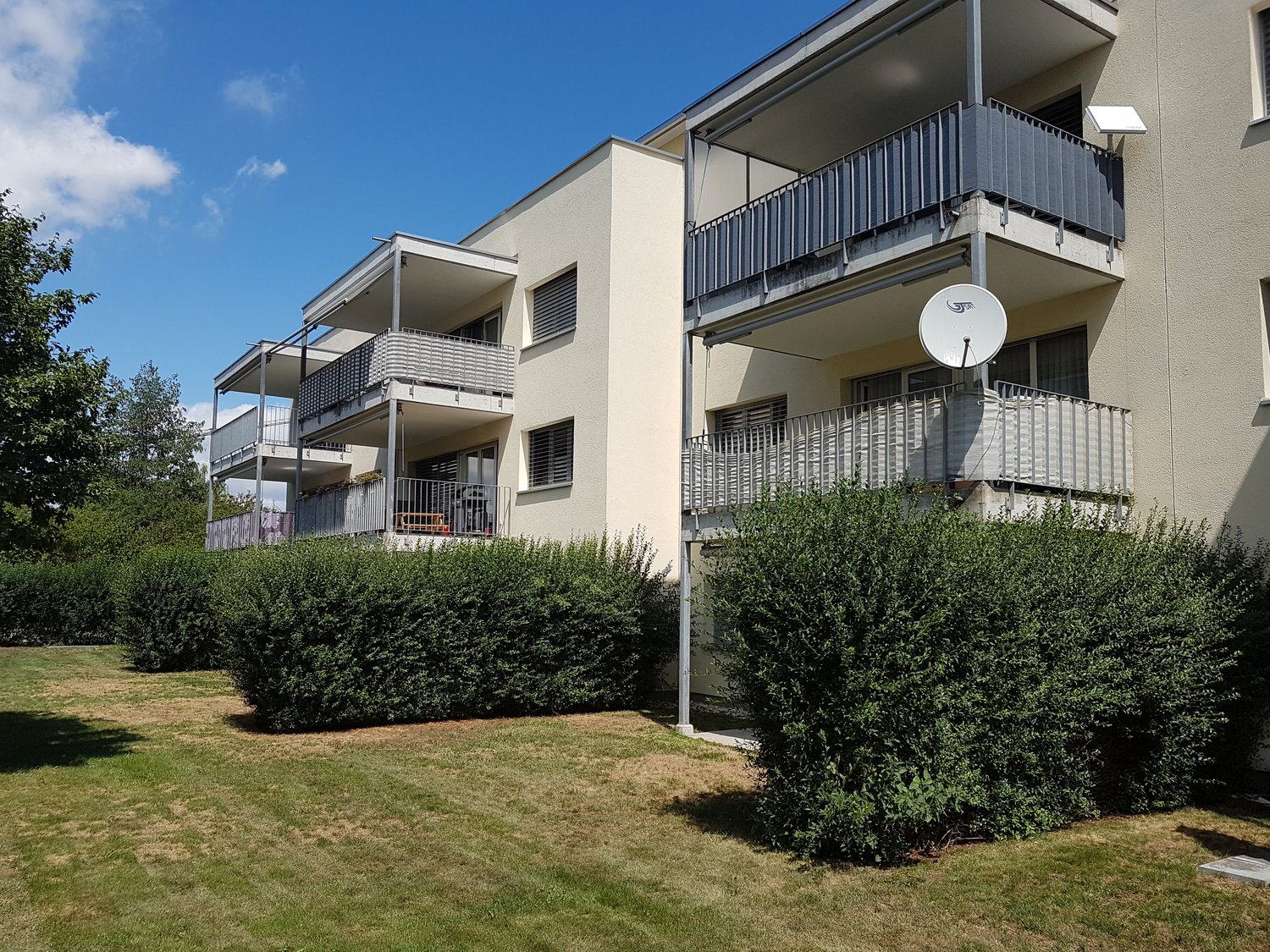 Multi-story building with multiple balconies, large windows, satellite dish.