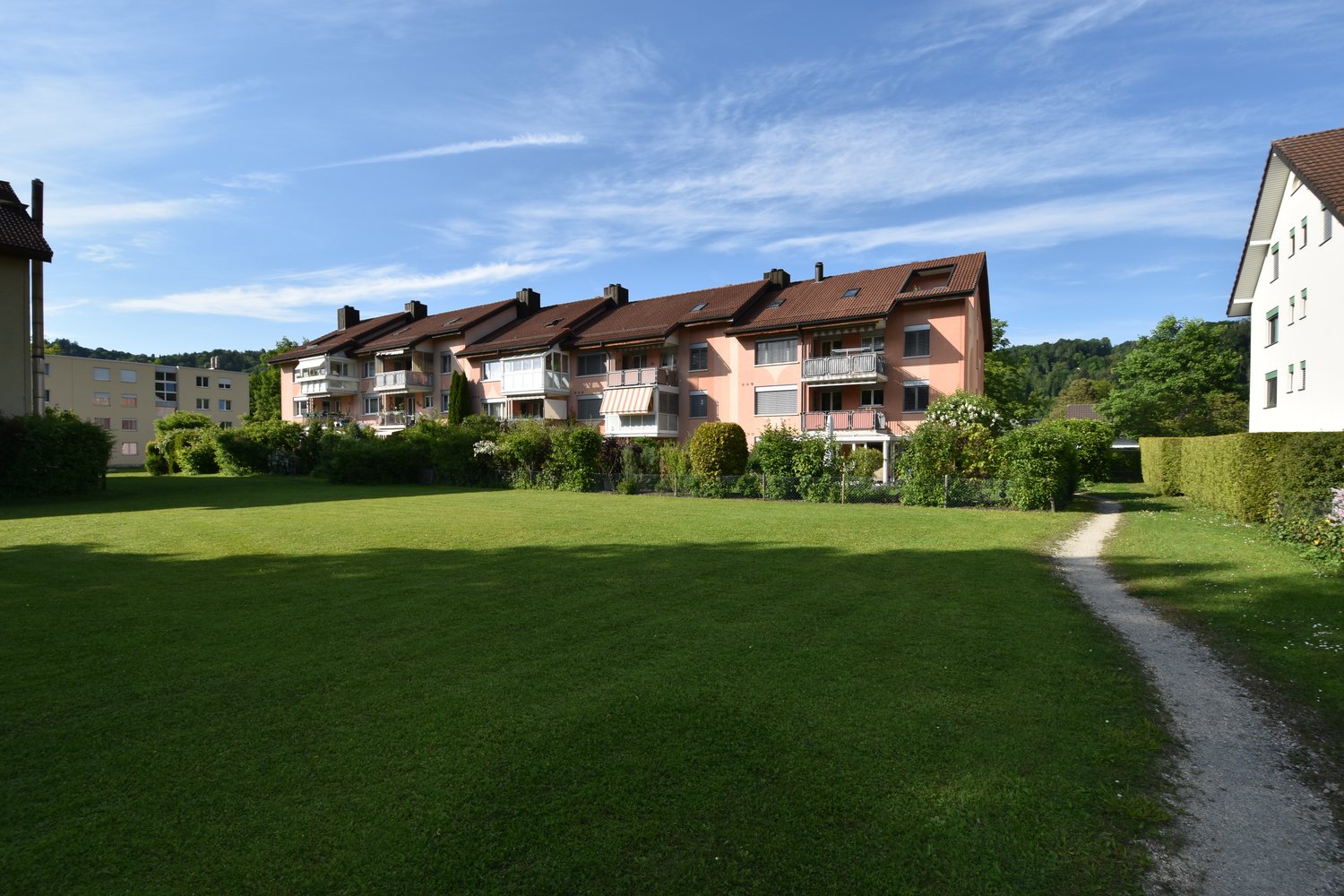 Apartment building with brown roofs, several floors, balconies, located in a green area with a large lawn