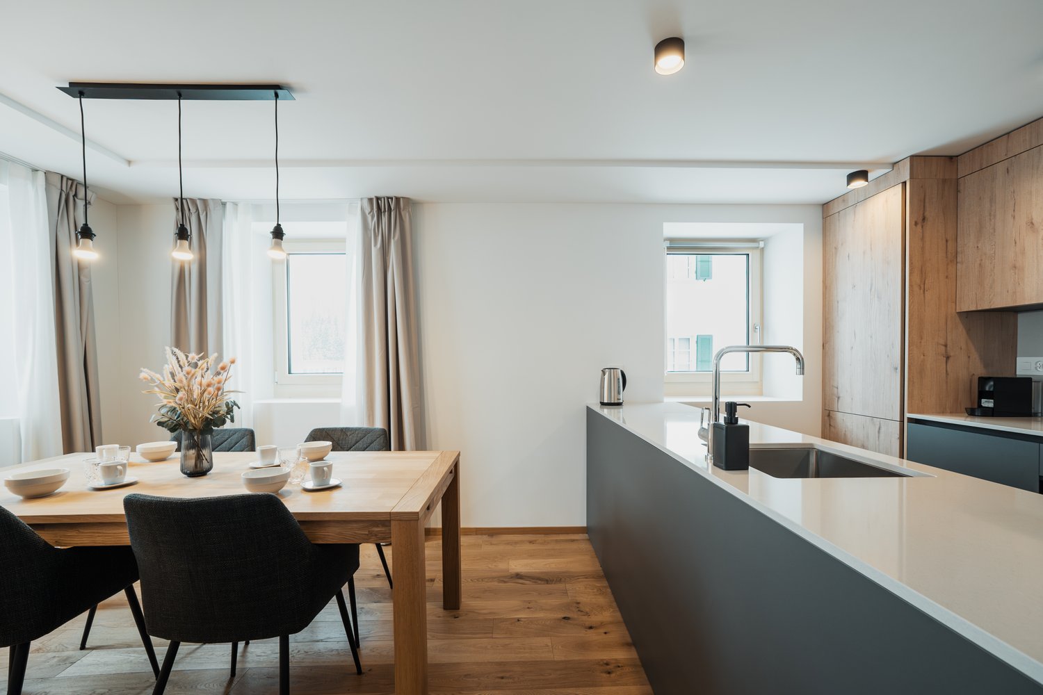 large table with chairs, modern kitchen island, white kitchen cabinets, light fixtures, window with view