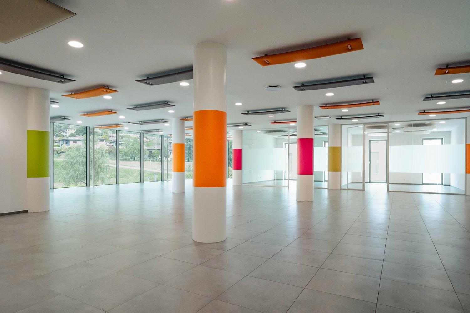 spacious room, white pillars, orange, green, and pink stripes on pillars, tiled floor, large windows, reflective surface