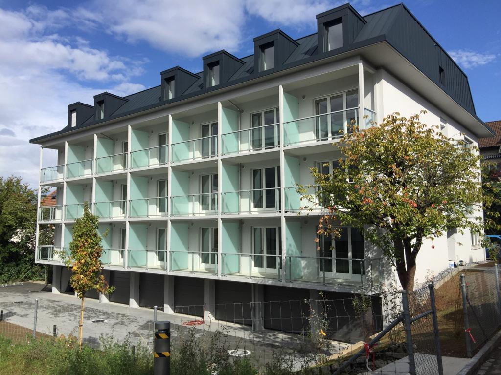 3-story apartment building with white exterior, glass balconies, and black roof dormers