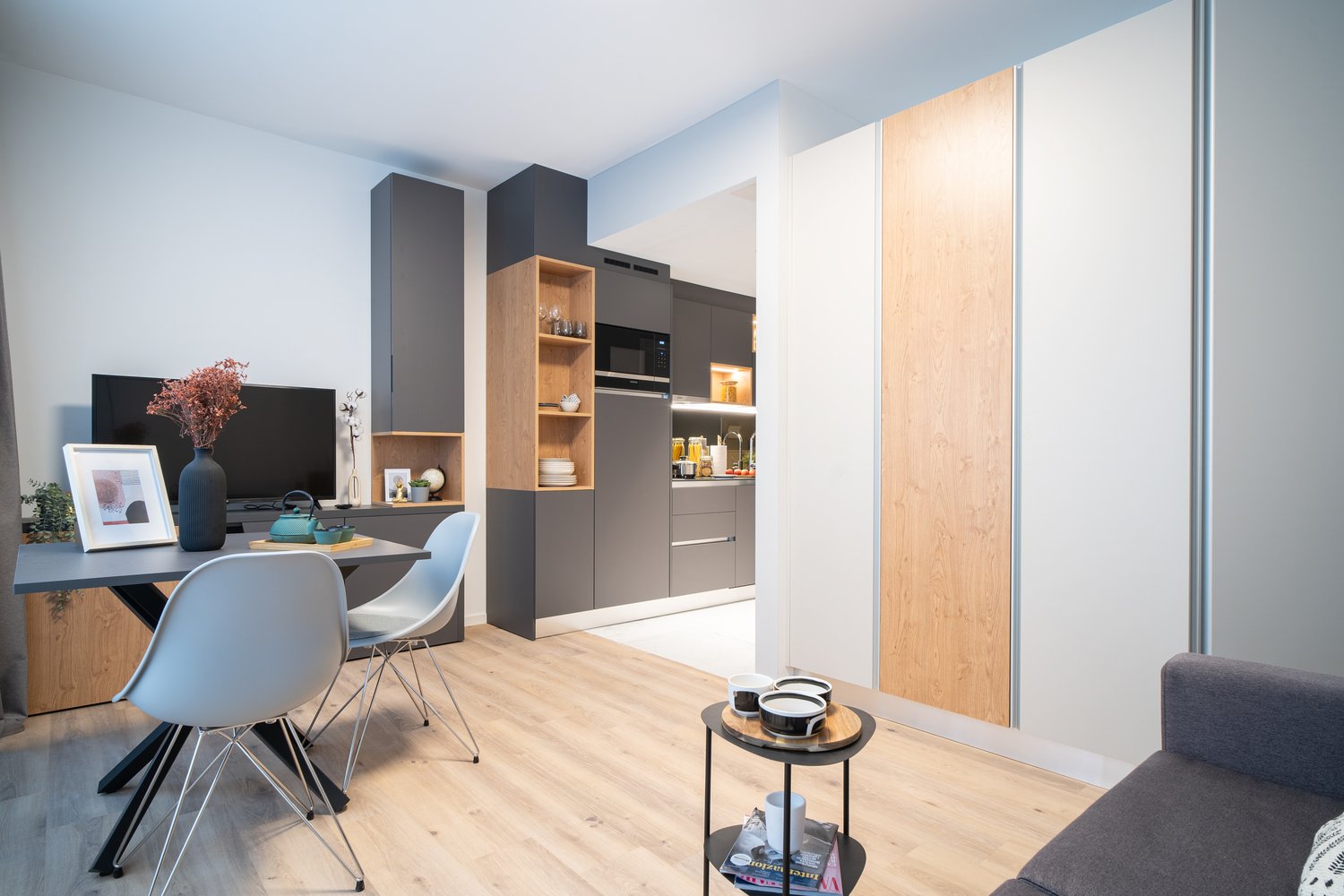 Modern kitchen with gray cabinets, wooden shelves, and built-in appliances including a dishwasher. Open concept living space with dining area and hardwood floors.