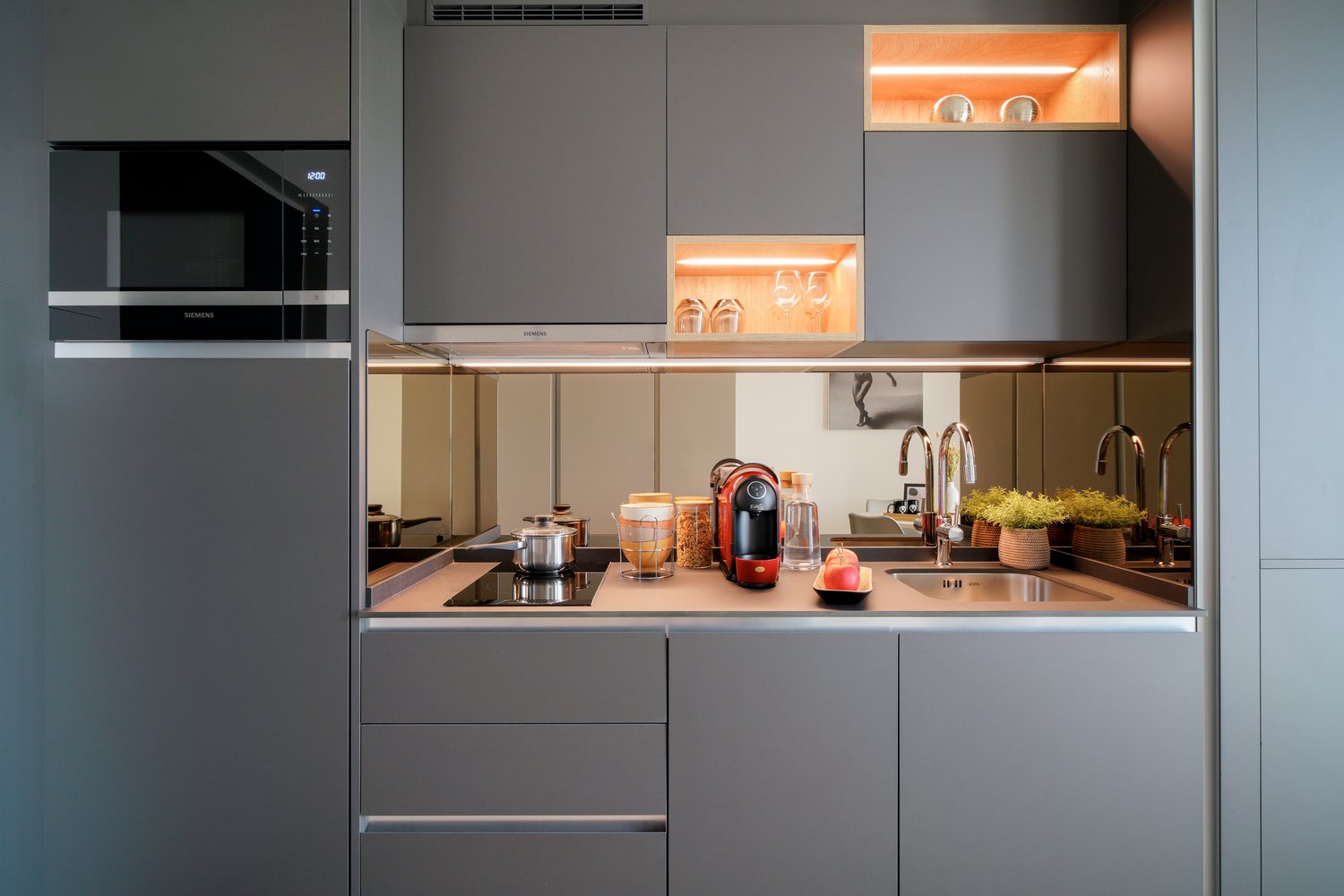 Modern kitchen with gray cabinets, wooden countertop, built-in Siemens microwave oven, various kitchen appliances and utensils, open shelving with decorative items