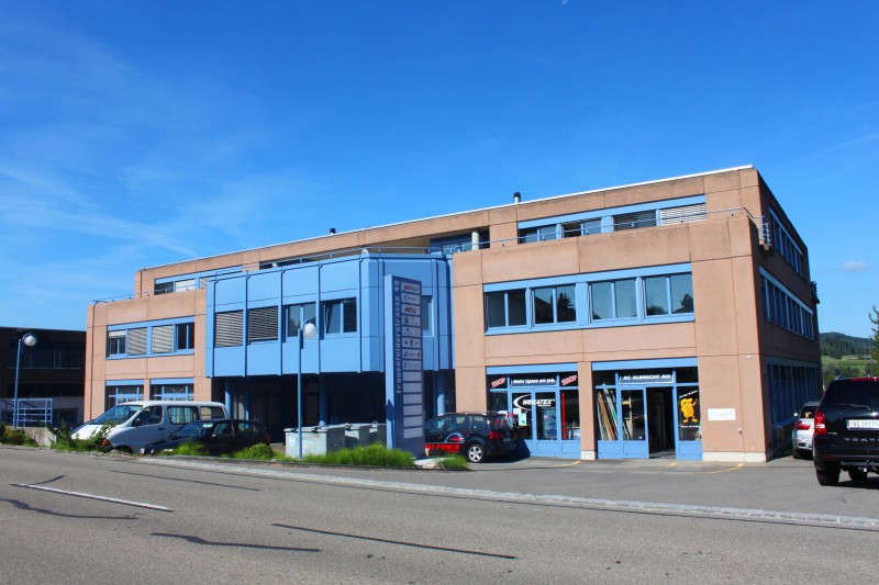Two-story building with blue and brown exterior, multiple windows, and a parking area in front.