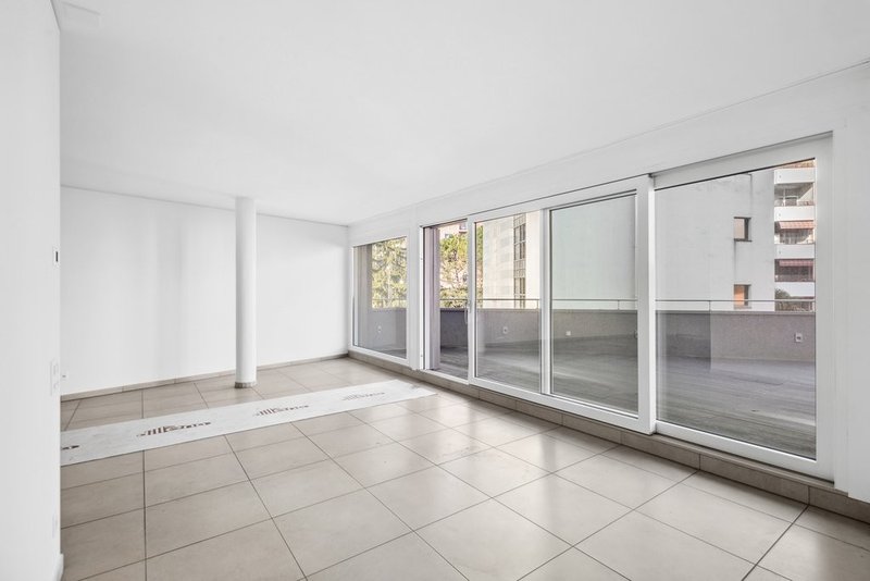 Empty room with white walls, tile floor, large windows and balcony