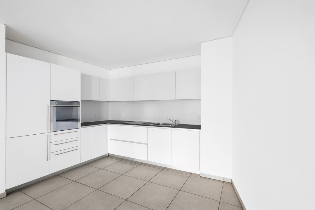 modern kitchen with white cabinets, black countertops, integrated oven, sink with faucet, tiled floor