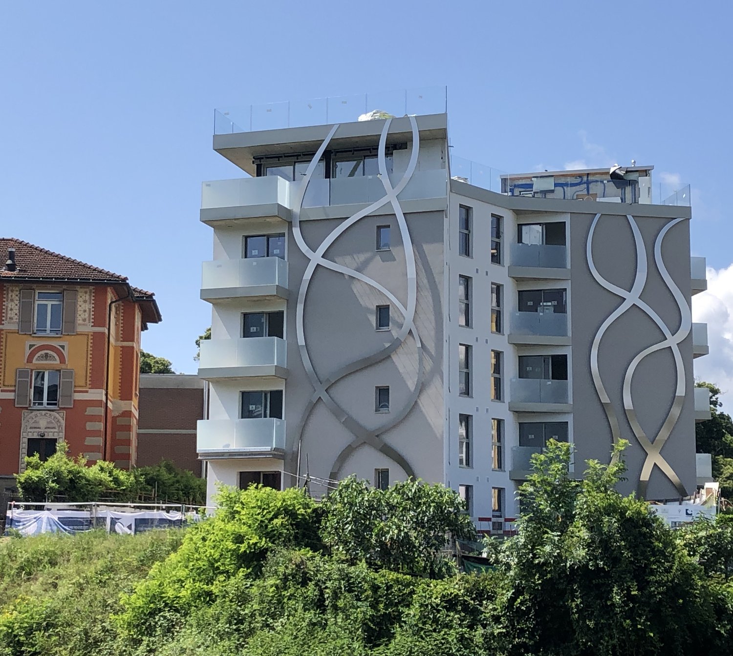 Building with modern architecture, large windows, multiple floors, white and gray facade, balconies on multiple levels, metal railings on balconies.