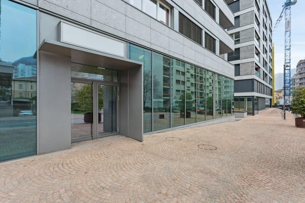Modern office building, glass facade, entrance with glass doors, brick pavement, central location, nearby construction