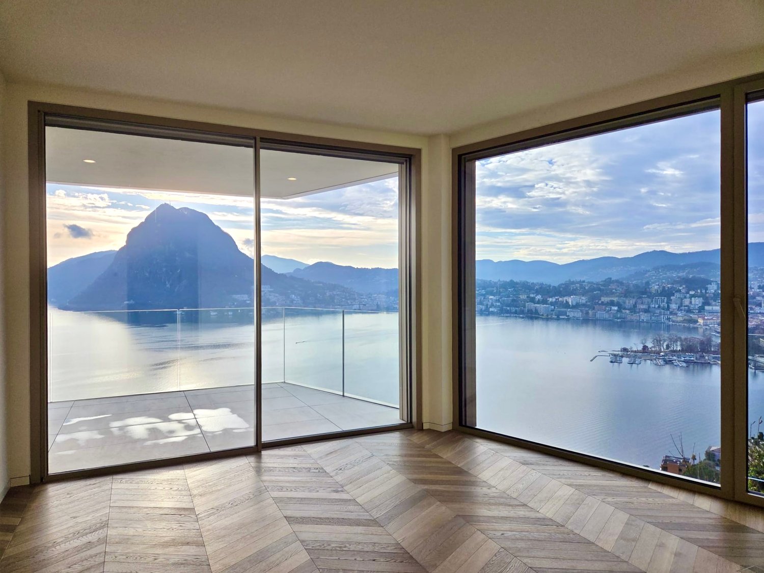 large glass windows, wooden floor, open balcony, view of lake and mountains