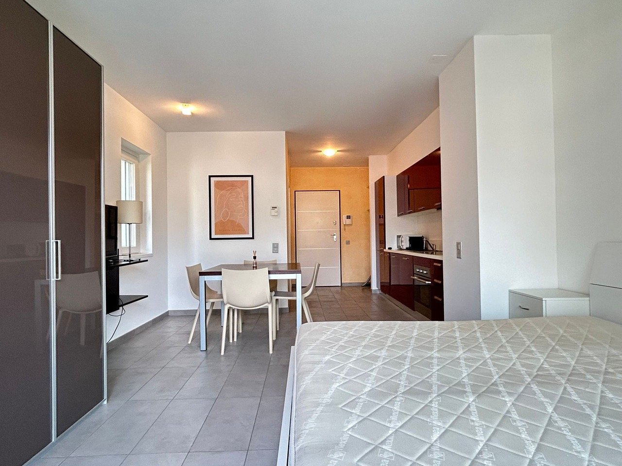 single bed, dining table with 4 chairs, wooden cabinets, wall painting, ceiling lights, white tiled floor