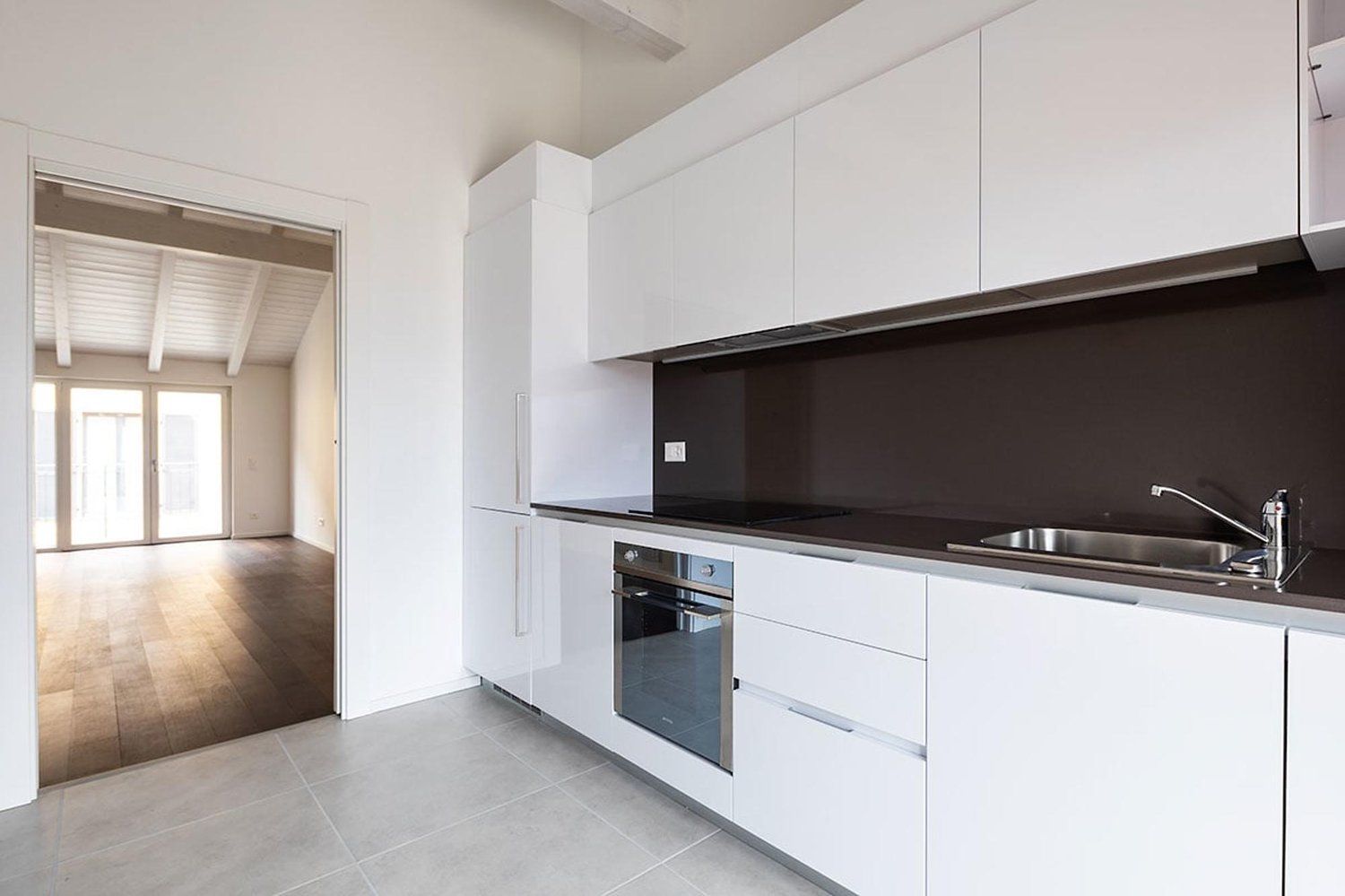 modern kitchen with white cabinets, gray tiled floor, stainless steel sink, oven, dishwasher, and a faucet