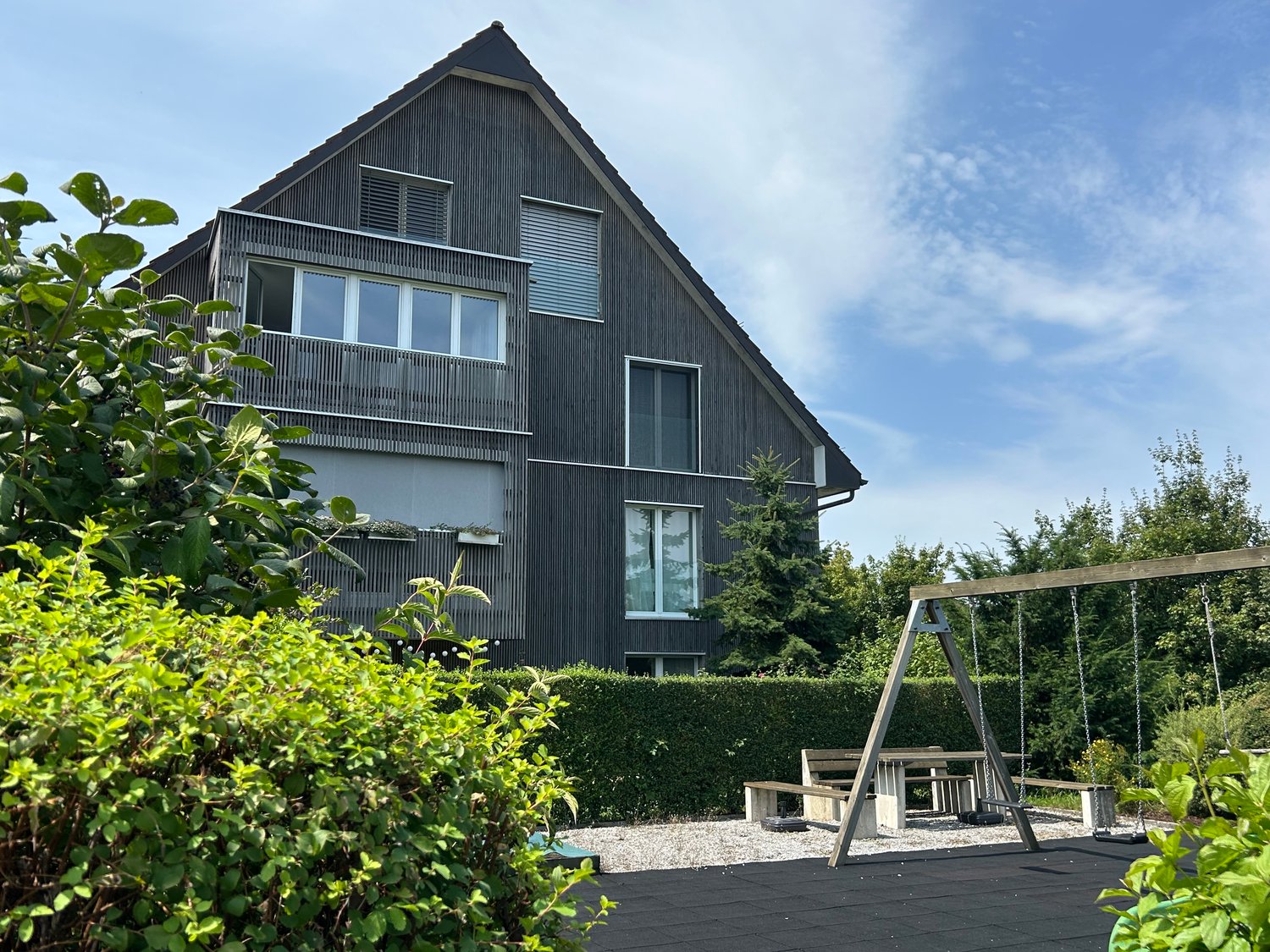 two-story house, modern design, surrounded by shrubs and trees, large windows, modern wooden swing
