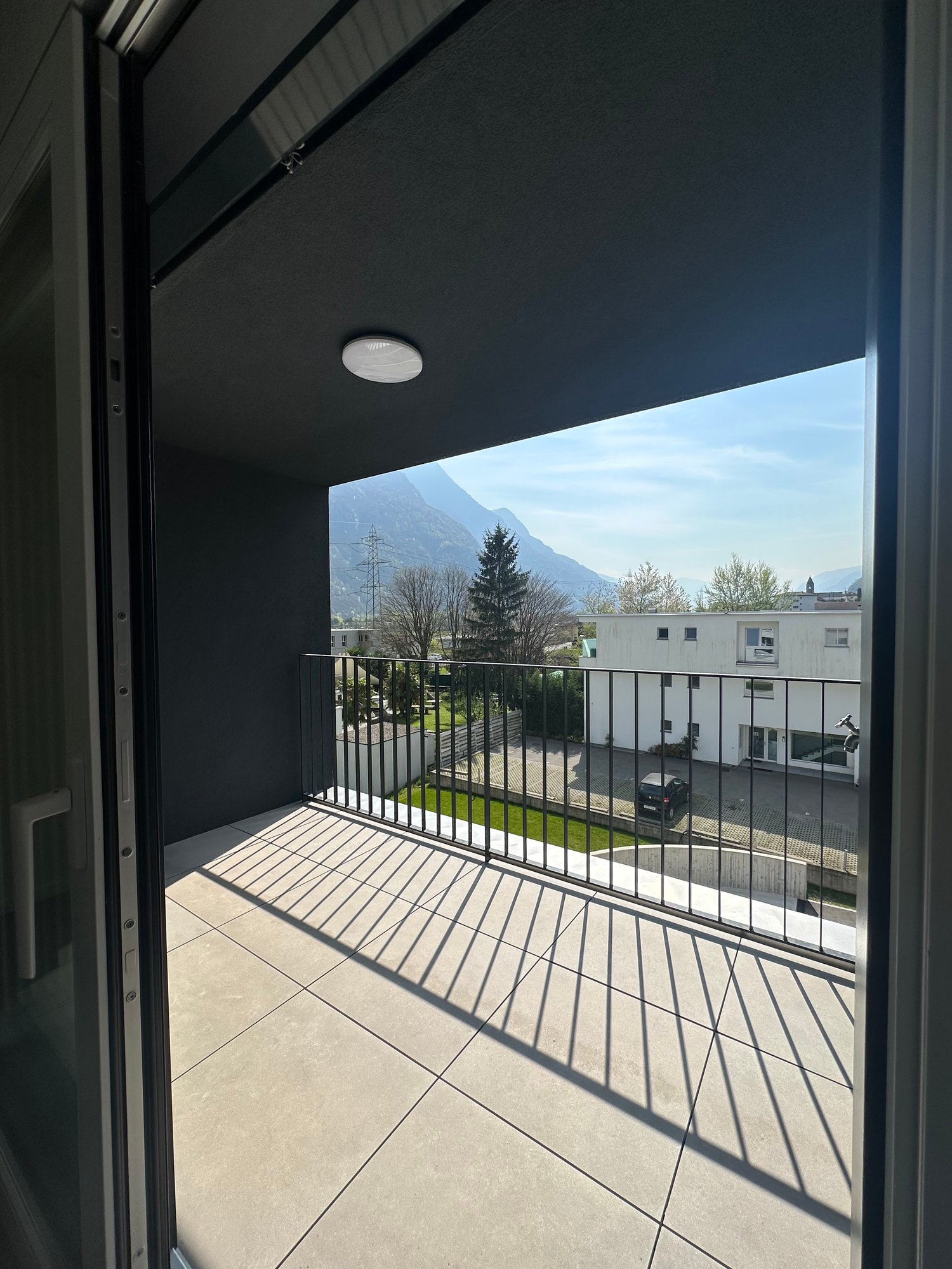 Balcony with black railings, tiled floor, view of car park and trees
