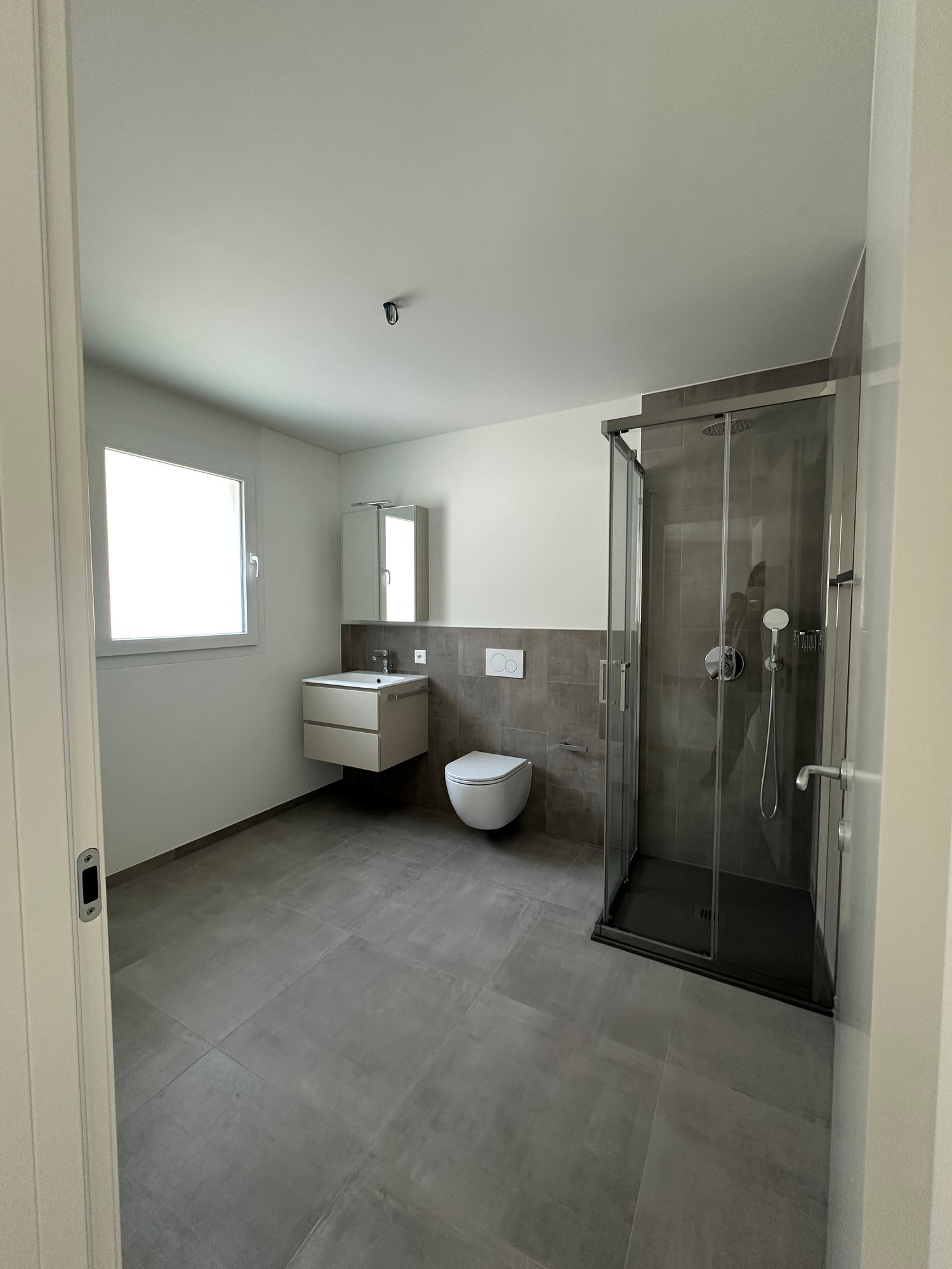 modern bathroom with glass shower, sink, toilet, window, gray tiles, white walls