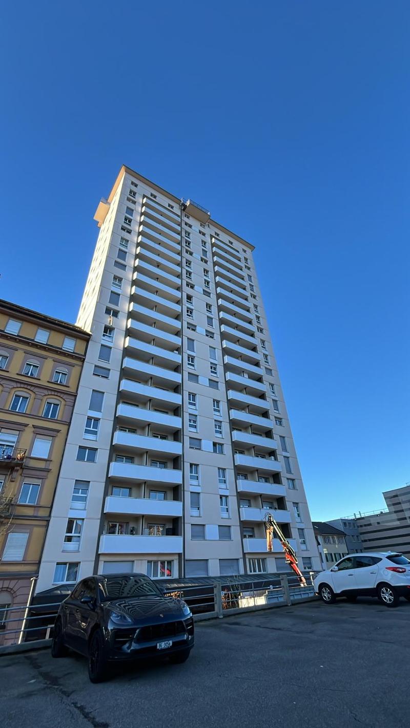 High-rise building with numerous balconies, modern architecture, two cars parked in front