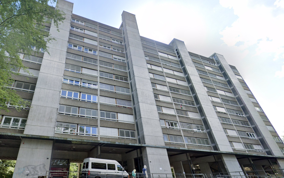 Concrete apartment building, multiple floors, numerous windows, large entrance with van parked