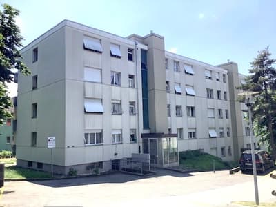 An apartment building with several windows, located at a roadside with parking area