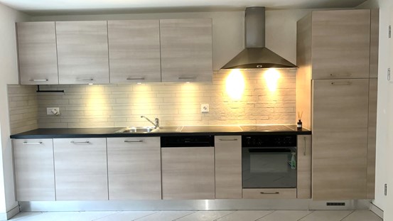 modern kitchen with oak-colored cabinetry, granite countertop, under-cabinet lighting, stainless steel sink, faucet, dishwasher, and integrated oven