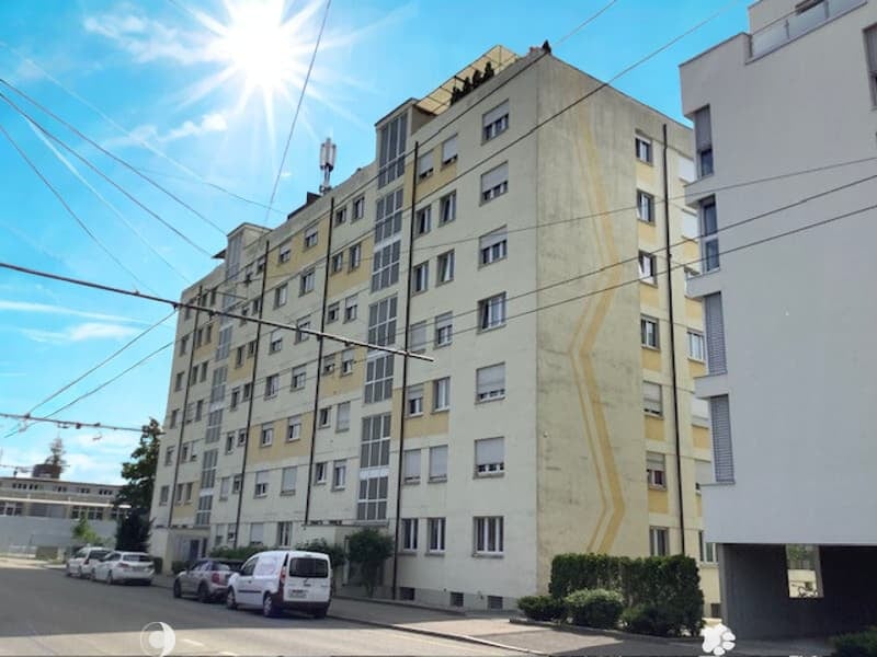 multi-story building, multiple windows, cars parked on the street, nearby greenery, clear blue sky