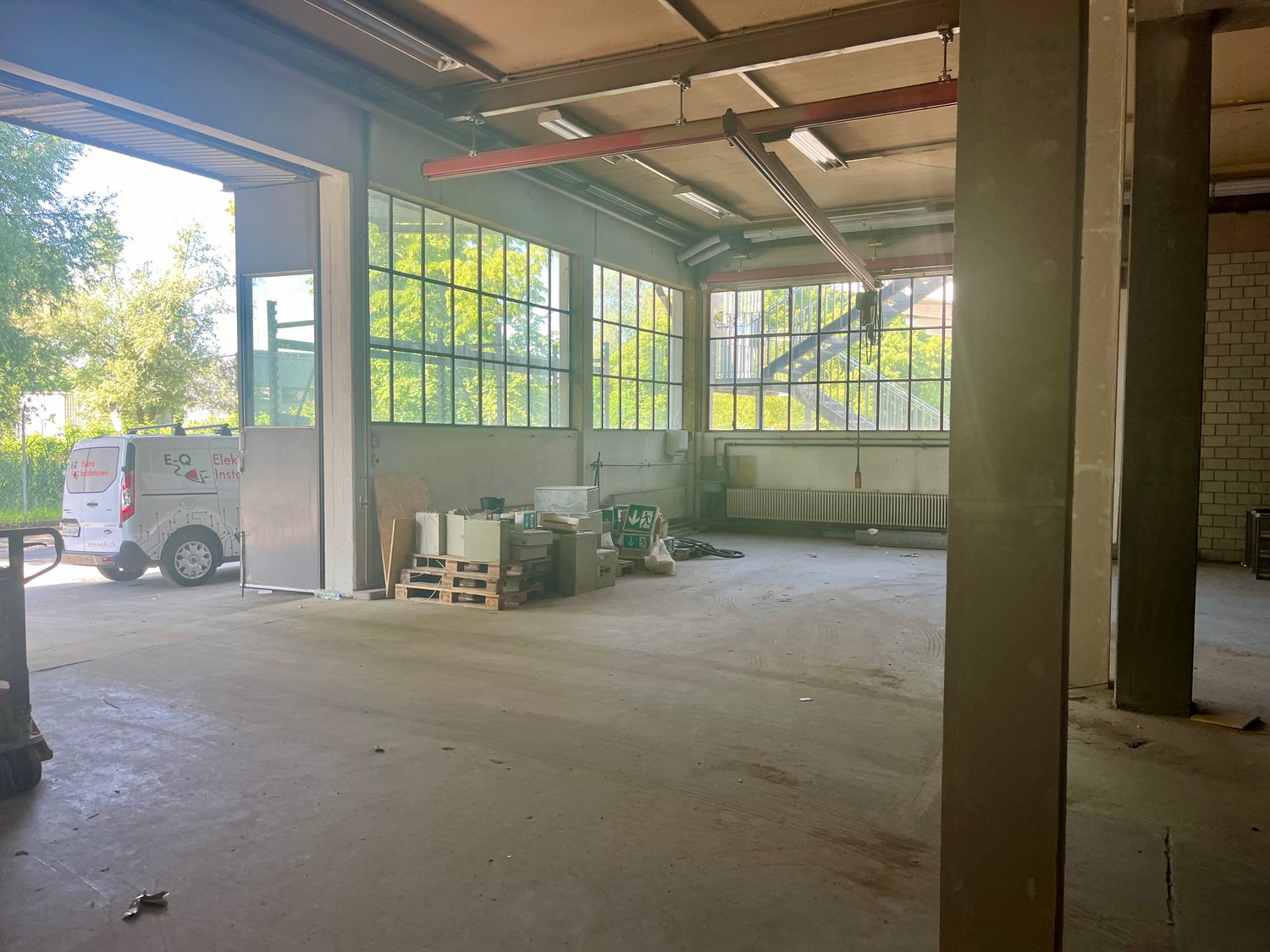 Large open space with concrete floor, brick walls, and large windows. There are some boxes and equipment visible, indicating it is being used as a storage or warehouse space.
